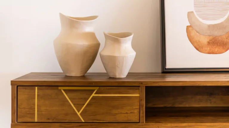 Vasijas de cerámica blanca sobre mueble de madera con líneas doradas. Cuadro abstracto enmarcado al lado.