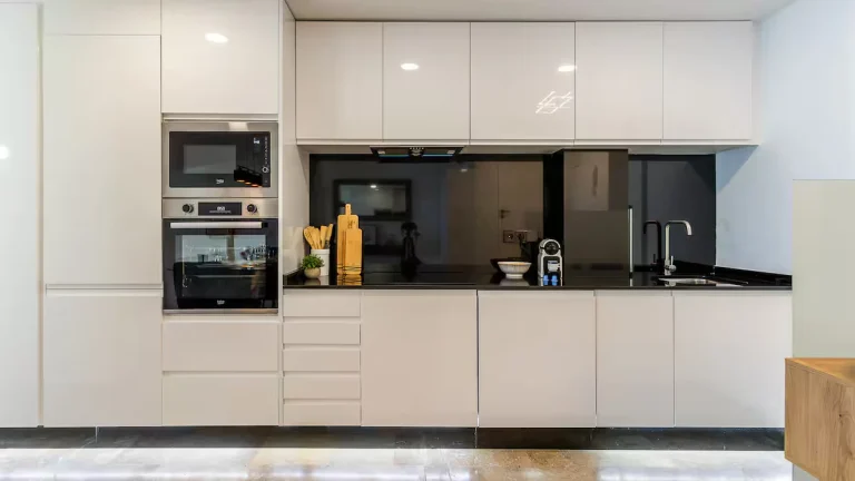 Cocina moderna blanca, electrodomésticos empotrados, encimera negra, tabla de cortar y utensilios junto a un fregadero.