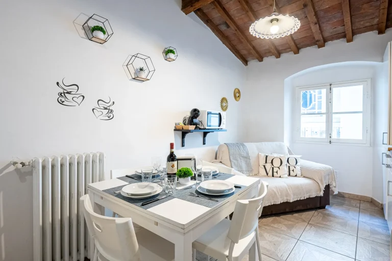 Sala de estar con mesa blanca puesta, estantería, sofá con cojines, decoración en pared blanca y techo de madera.