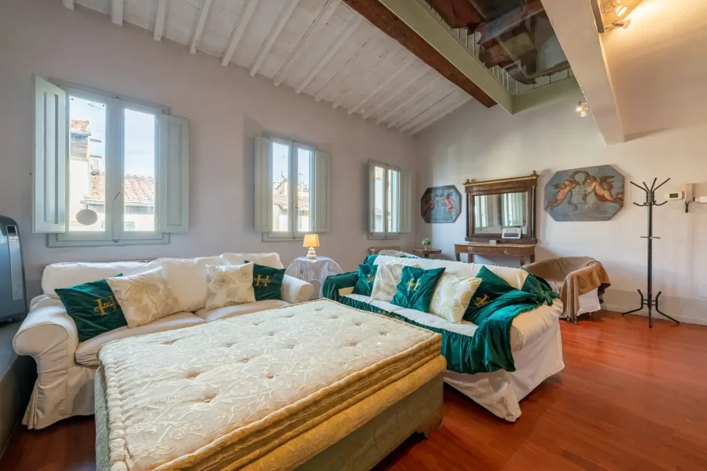 Sala de estar luminosa con sofás blancos, cojines verdes, paredes claras, suelo de madera y cuadros de ángeles. Ventanas amplias.