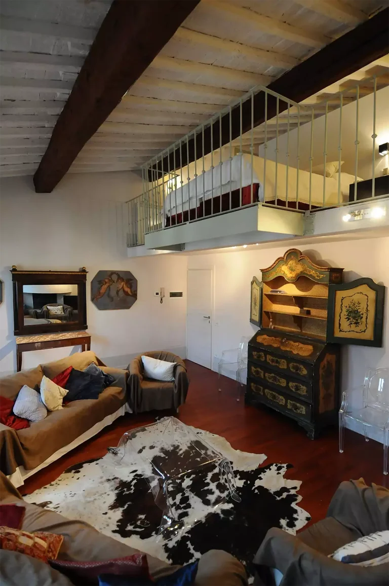 Sala de estar con sofá grande, sillón, alfombra de piel, mueble antiguo, cama en un altillo, techo con vigas de madera.