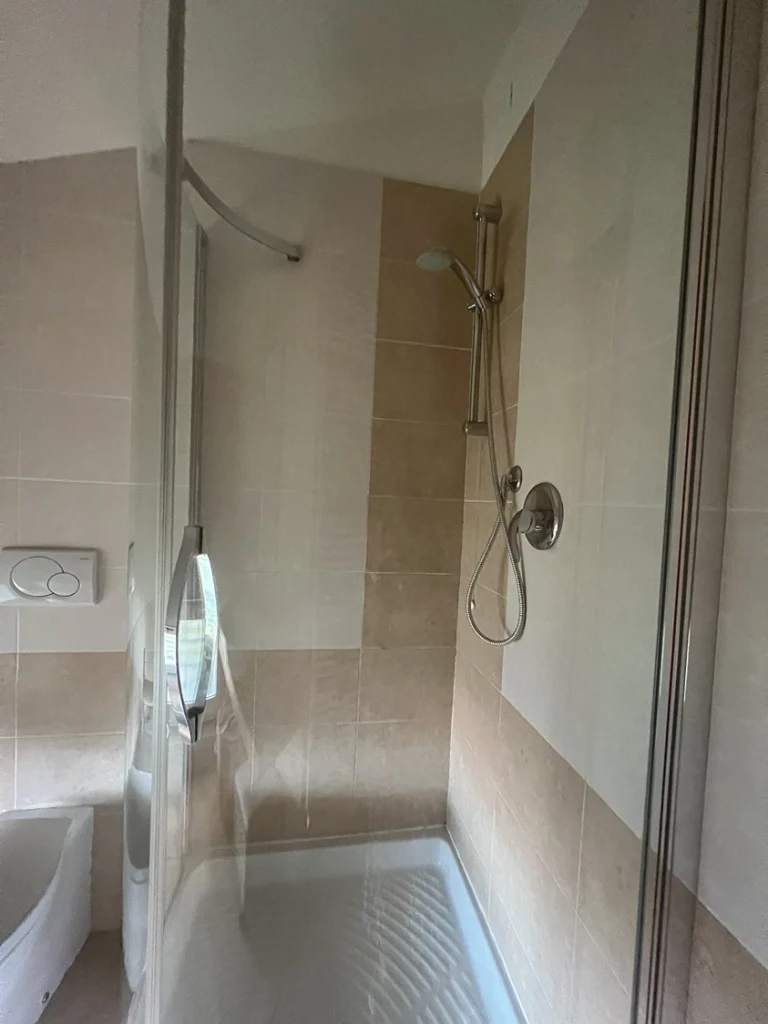 Baño moderno con ducha de cristal, inodoro y bidé. Lavabo sobre encimera y ventana baja con vidrio esmerilado. Iluminación empotrada en el techo.