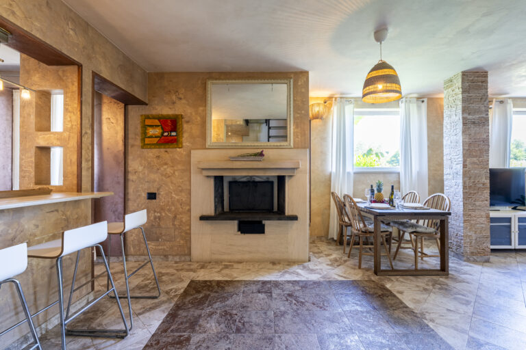 Sala de estar con chimenea central, mesa de comedor, sillas de madera, lámpara colgante y decoración neutra.