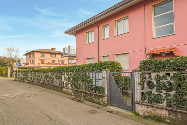 Edificios residenciales rosados con ventanas grandes, cerca de una calle tranquila. Cerca de arbustos y buzones metálicos.