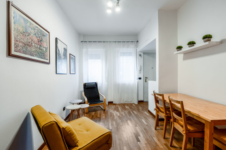 Sala de estar con suelo de madera, paredes blancas, sofás modernos, mesa de comedor de madera y cuadros en la pared.