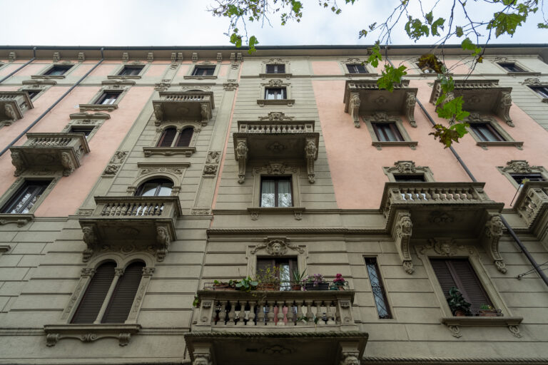 Edificio de estilo clásico con paredes rosas y detalles ornamentales en gris, balcones con barandillas y ventanas altas.
