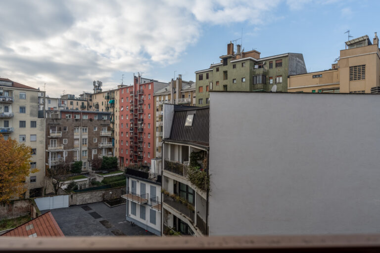 Edificios residenciales de colores, cielo nublado, árboles y antenas en techos en un vecindario urbano.