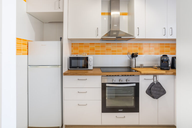 Cocina moderna con frigorífico blanco, microondas, horno, estufa y campana. Decoración con azulejos naranjas y encimera de madera.
