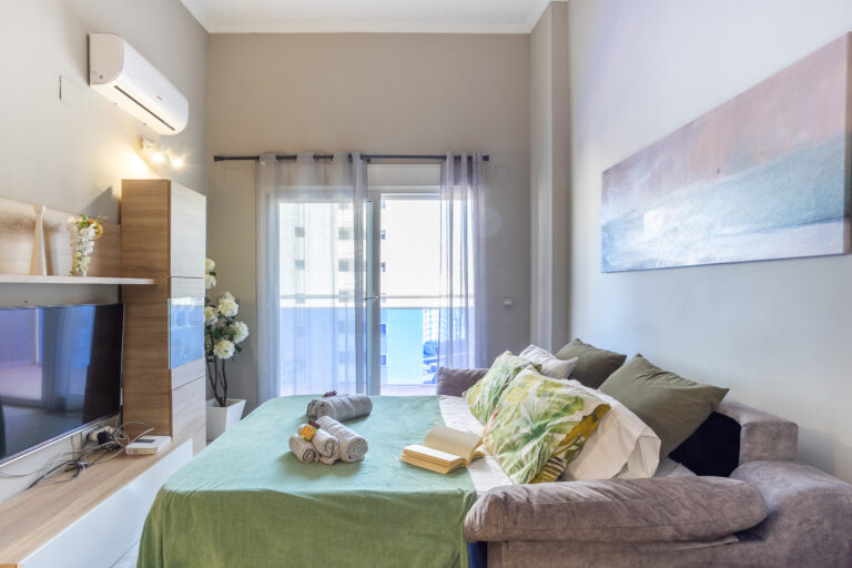 Dormitorio moderno con cama verde, cojines coloridos y arte abstracto en la pared. Luz natural entra por la ventana con cortinas.