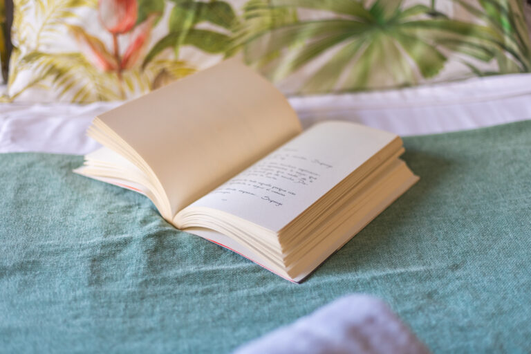 Libro abierto sobre tela verde y cama blanca, fondo con diseño de hojas tropicales en tonos verdes y rojos.