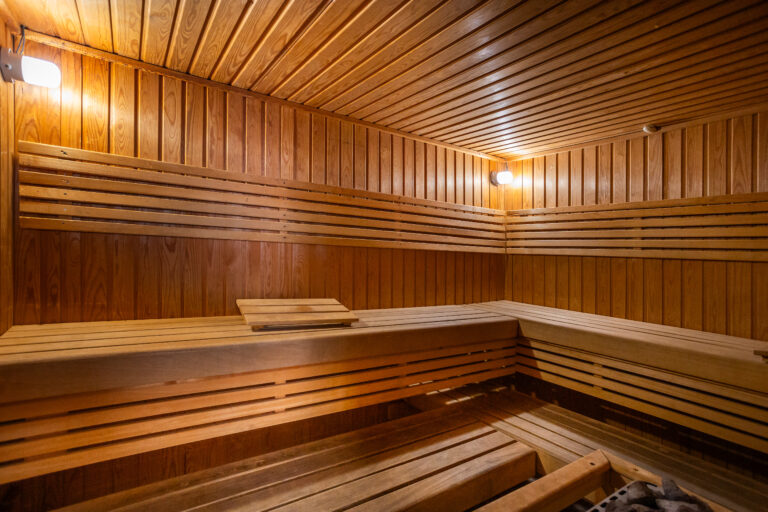 Sauna de madera clara con bancos escalonados y luces suaves en las paredes. Ambiente cálido y acogedor.