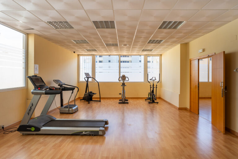 Sala de gimnasio con máquinas de ejercicio: cintas de correr, bicicleta estática y elíptica, en un espacio amplio y luminoso.
