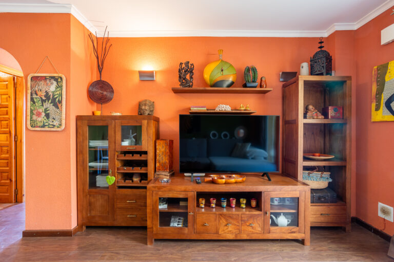 Sala de estar con paredes naranjas, muebles de madera, televisor, estanterías decorativas y adornos diversos.
