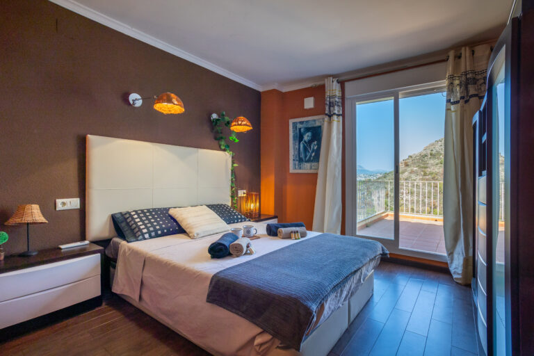 Dormitorio acogedor con cama doble, lámparas cálidas, pared marrón, una puerta corrediza y vistas montañosas.