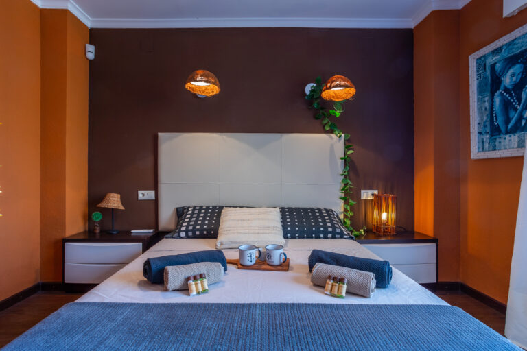 Moderna habitación con paredes marrones, cama de gran cabecera, lámparas colgantes y decoración cálida.