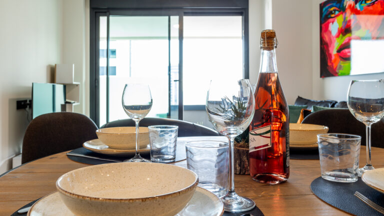 Mesa con platos de cerámica, copas de vino, botella de vino rosado y decoración moderna en el fondo.