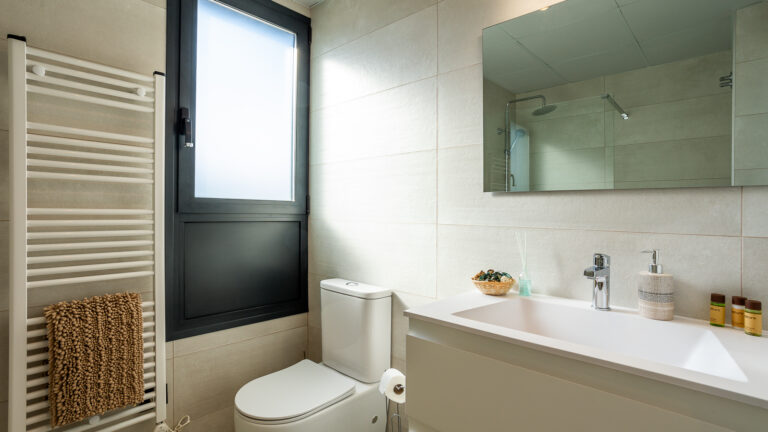 Cuarto de baño con ventana esmerilada, espejo amplio, lavabo blanco, toallero blanco y taza de inodoro moderna.