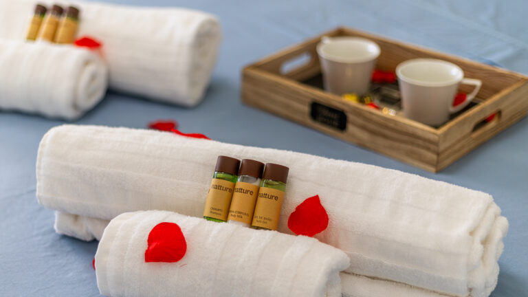 Toallas blancas enrolladas, pétalos rojos dispersos. Frascos de champú y gel de baño, bandeja con tazas blancas.