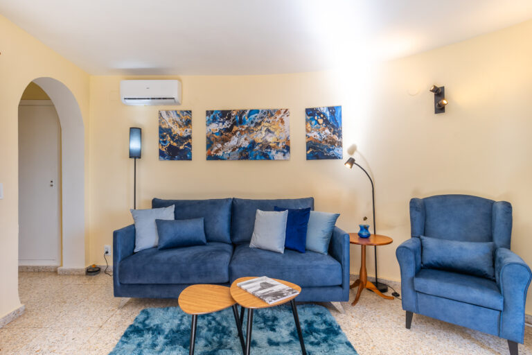 Sala de estar con sofá y sillón azul, alfombra a juego, mesa de centro y arte abstracto azul y dorado en la pared.