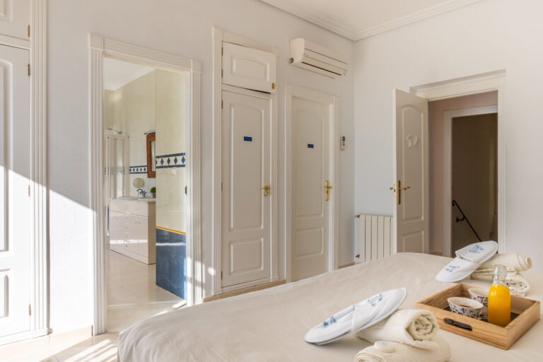 Habitación luminosa con puerta abierta al baño con azulejos. Cama con bandeja, jugo, tazas y toallas. Aire acondicionado arriba.